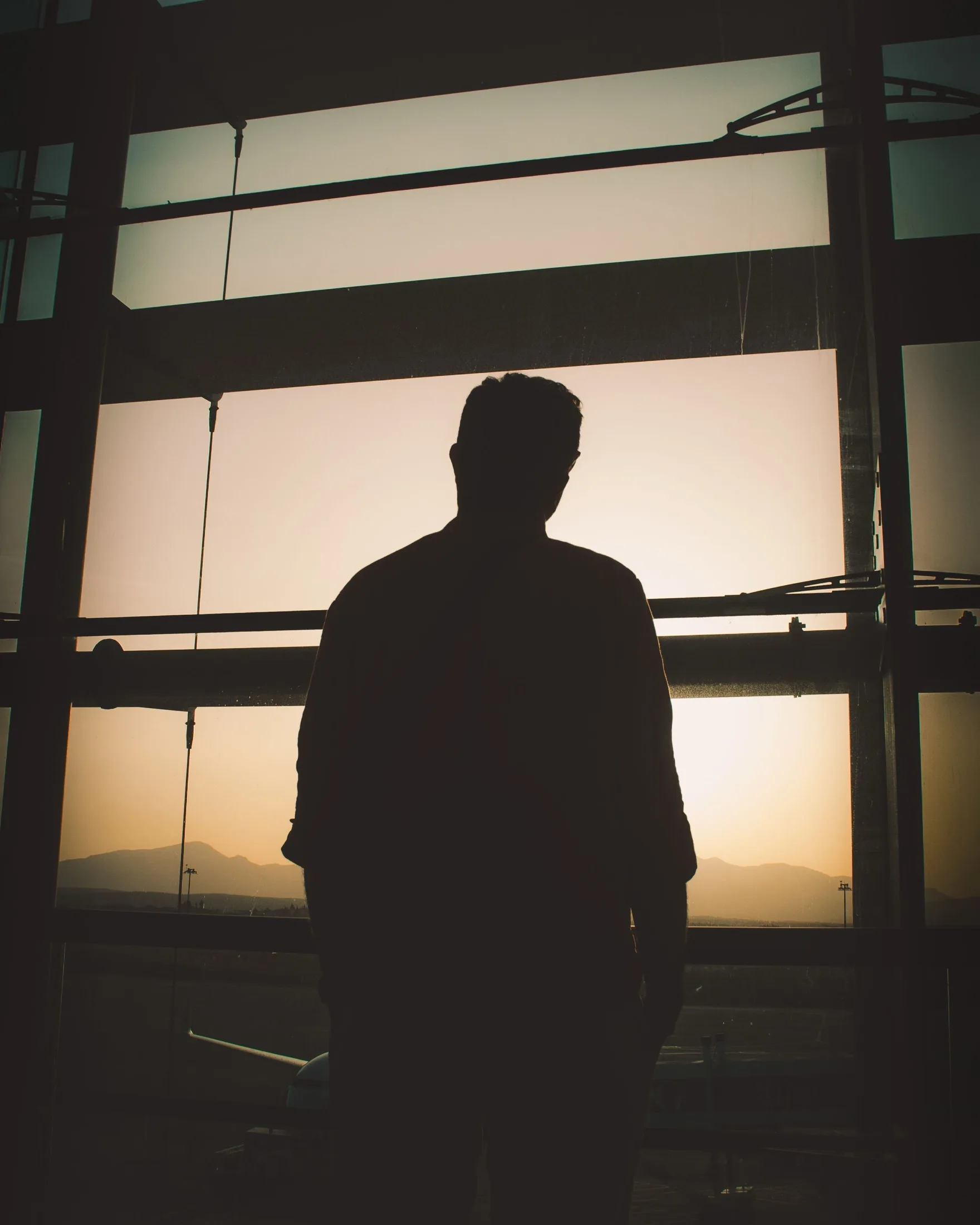 A traveler pausing in an airport terminal at sunset, mid-relocation